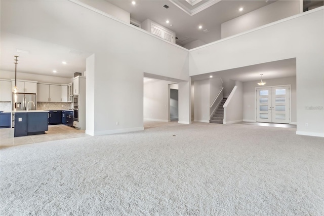 unfurnished living room featuring a high ceiling, light colored carpet, and sink