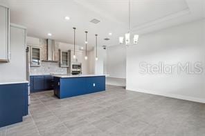 kitchen featuring blue cabinetry, a center island, hanging light fixtures, wall chimney range hood, and decorative backsplash