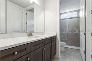 bathroom with tile patterned flooring, a tile shower, vanity, and toilet