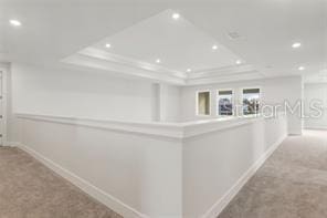 hallway with a raised ceiling and light carpet