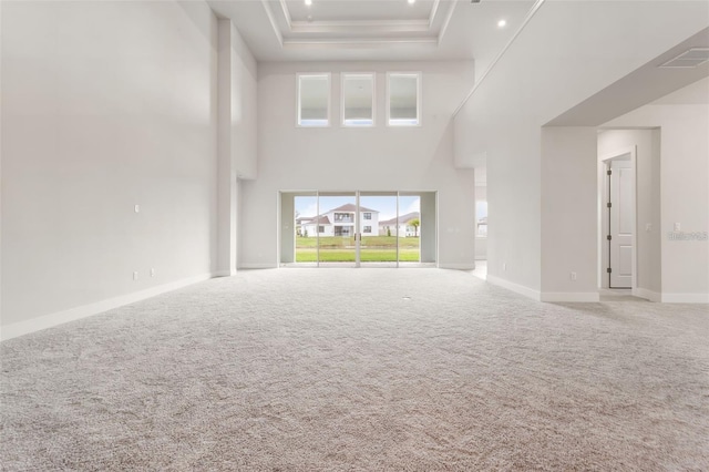 unfurnished living room featuring carpet, a high ceiling, and a raised ceiling