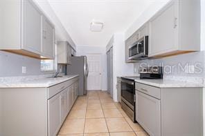 kitchen with gray cabinets, sink, light tile patterned floors, and appliances with stainless steel finishes