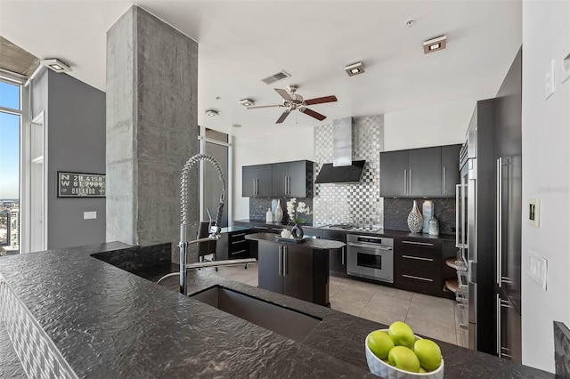 kitchen with stainless steel oven, wall chimney exhaust hood, a center island, backsplash, and kitchen peninsula