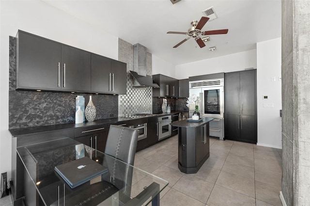 kitchen featuring appliances with stainless steel finishes, tasteful backsplash, wall chimney exhaust hood, light tile patterned floors, and a kitchen island