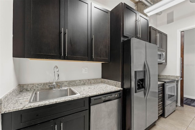 kitchen with light tile patterned flooring, stainless steel appliances, light stone countertops, and sink