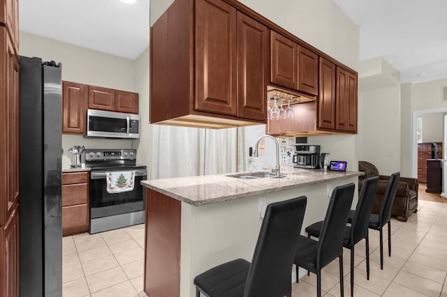 kitchen with kitchen peninsula, light stone countertops, a breakfast bar, stainless steel appliances, and light tile patterned floors