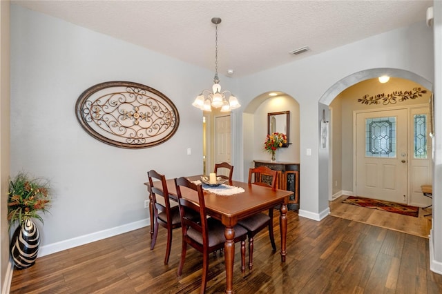 dining area with a textured ceiling, dark hardwood / wood-style flooring, and an inviting chandelier