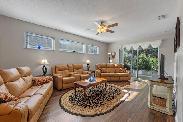 living room with a textured ceiling, ceiling fan, and dark wood-type flooring