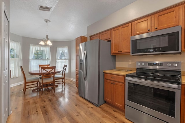 kitchen with decorative light fixtures, a textured ceiling, appliances with stainless steel finishes, a notable chandelier, and light hardwood / wood-style floors