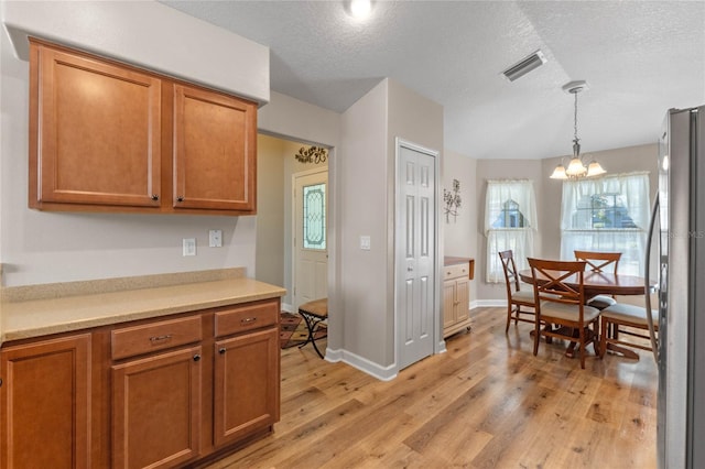 kitchen with decorative light fixtures, light hardwood / wood-style flooring, stainless steel fridge, a textured ceiling, and a notable chandelier