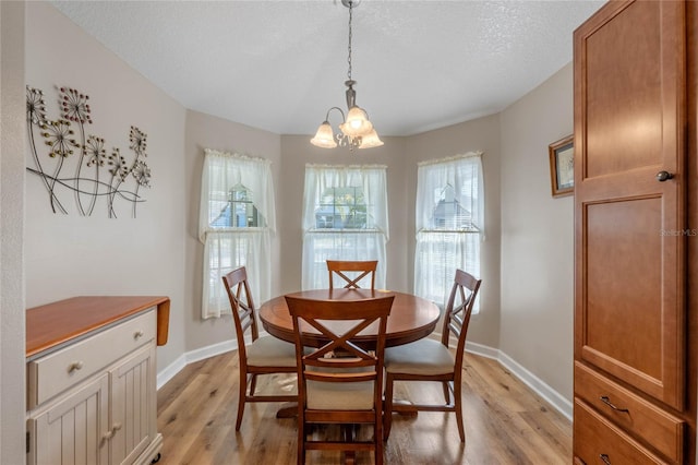 dining area featuring light wood-type flooring, a textured ceiling, and a chandelier