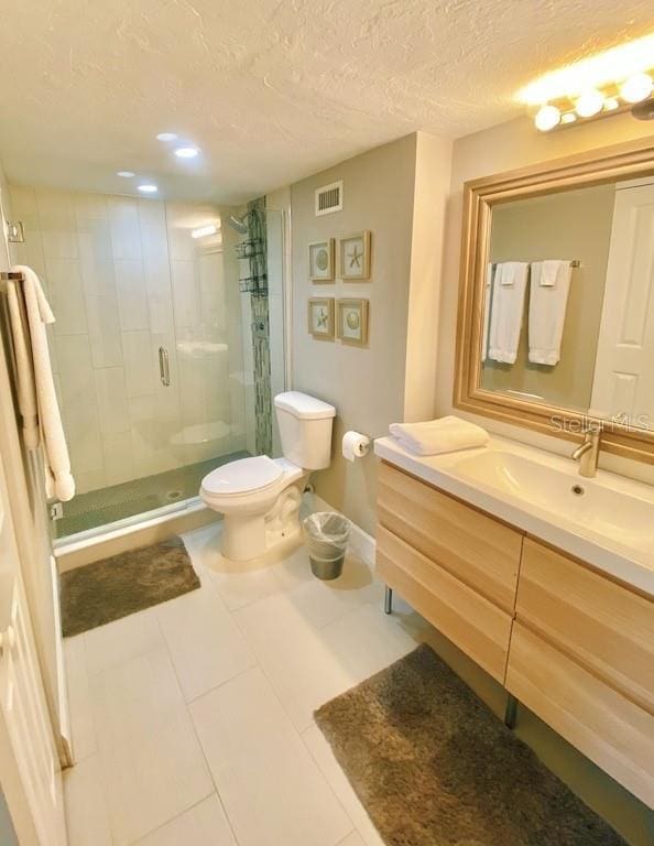 bathroom featuring tile patterned floors, a textured ceiling, toilet, a shower with door, and vanity