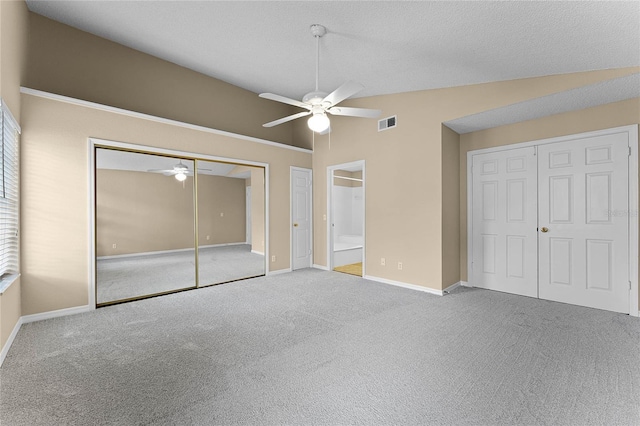 unfurnished bedroom with ceiling fan, ensuite bathroom, light colored carpet, vaulted ceiling, and two closets