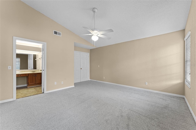 unfurnished bedroom with a closet, light colored carpet, ceiling fan, and ensuite bathroom