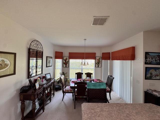 dining space with plenty of natural light, light colored carpet, and an inviting chandelier