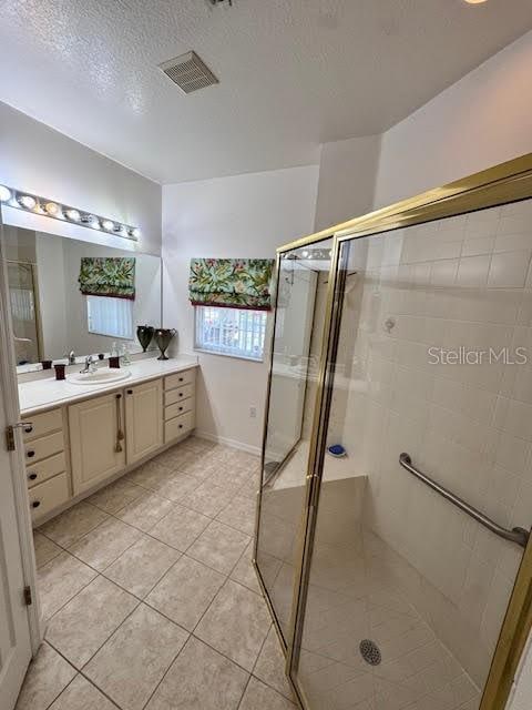 bathroom with tile patterned floors, vanity, a shower with door, and a textured ceiling