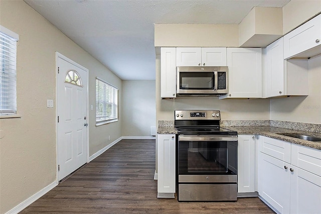 kitchen with dark stone counters, stainless steel appliances, white cabinetry, and dark wood-type flooring