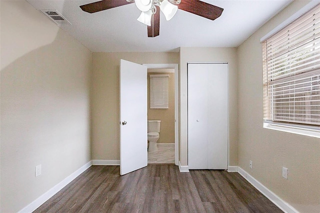 unfurnished bedroom with a closet, ensuite bath, ceiling fan, and dark wood-type flooring