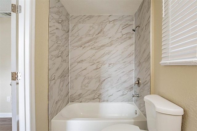 bathroom featuring a textured ceiling, tiled shower / bath combo, and toilet