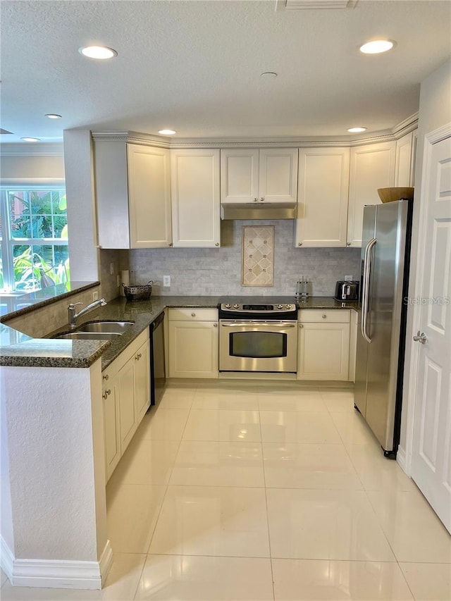 kitchen featuring sink, stainless steel appliances, kitchen peninsula, dark stone counters, and decorative backsplash