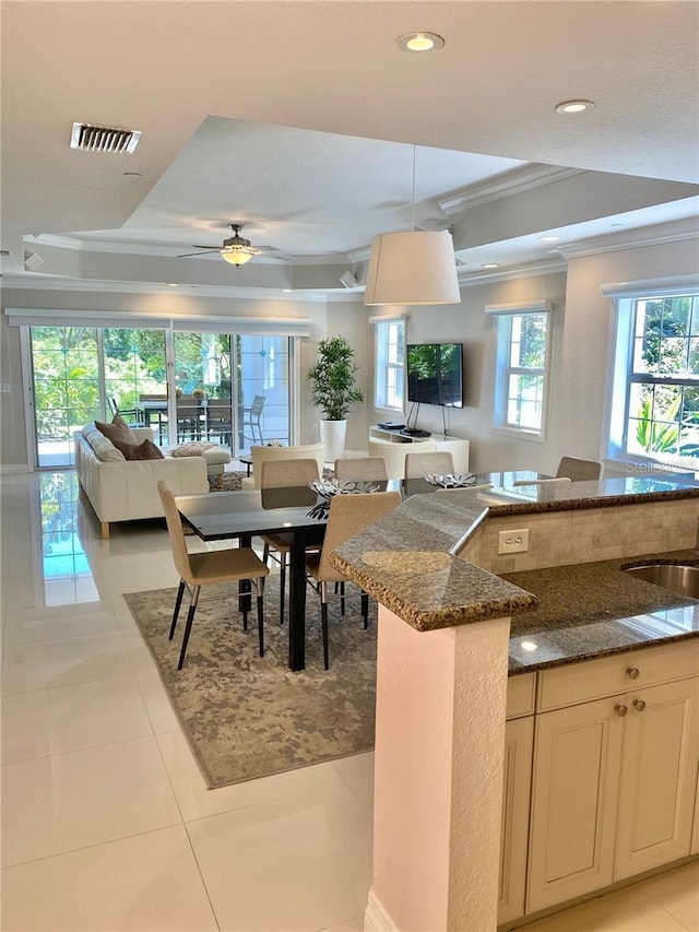 kitchen featuring light tile patterned floors, visible vents, open floor plan, dark stone countertops, and crown molding