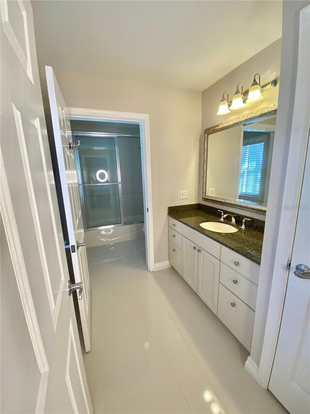 bathroom featuring baseboards, combined bath / shower with glass door, and vanity