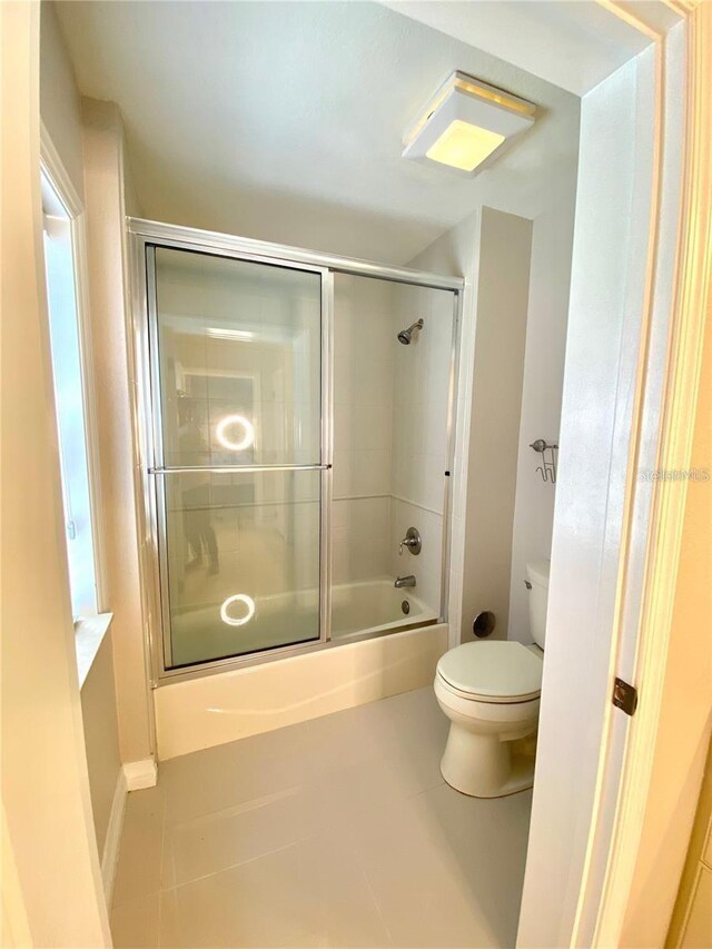 bathroom with shower / bath combination with glass door, toilet, and tile patterned floors