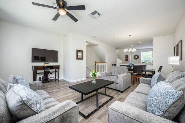 living room featuring ceiling fan with notable chandelier and light wood-type flooring