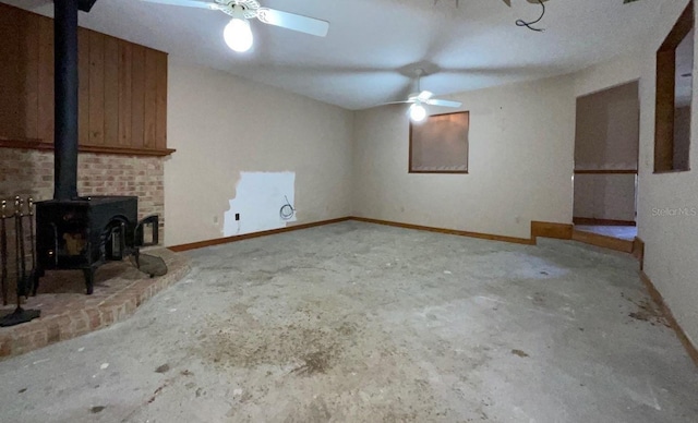 unfurnished living room featuring a wood stove, ceiling fan, and concrete floors