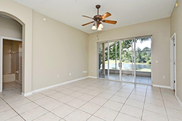 empty room featuring arched walkways, light tile patterned flooring, a ceiling fan, and baseboards