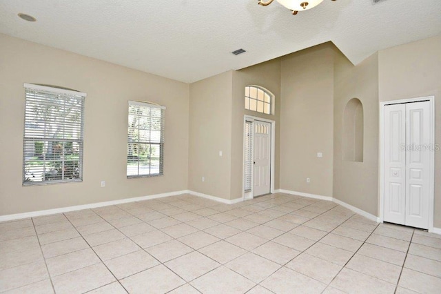 spare room featuring light tile patterned floors, baseboards, visible vents, and a textured ceiling