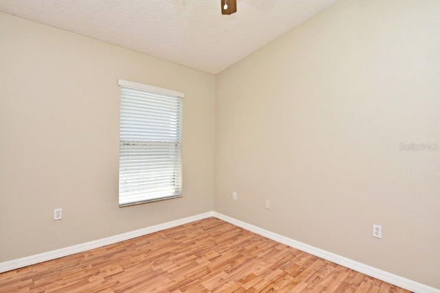 empty room with light wood-style flooring, baseboards, vaulted ceiling, and a textured ceiling