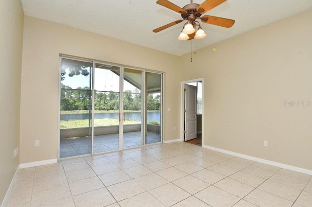 empty room featuring ceiling fan, a water view, light tile patterned flooring, and baseboards