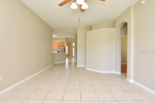 unfurnished room with a ceiling fan, arched walkways, baseboards, and light tile patterned floors