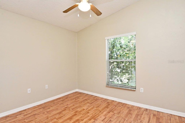 empty room with lofted ceiling, a textured ceiling, a ceiling fan, baseboards, and light wood-style floors