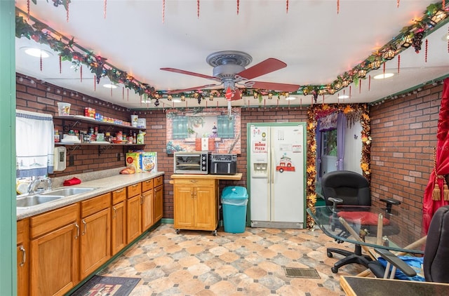 kitchen featuring ceiling fan, white fridge with ice dispenser, sink, and brick wall