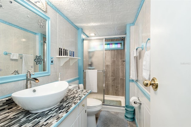 bathroom with walk in shower, vanity, toilet, and tile walls