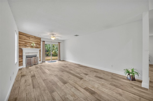 unfurnished living room featuring wood walls, a large fireplace, ceiling fan, and light wood-type flooring