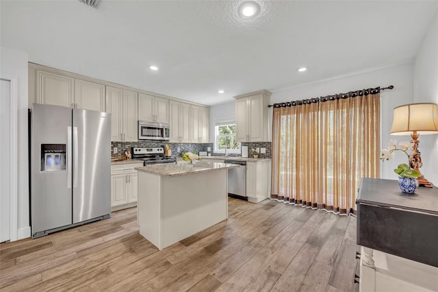 kitchen with light hardwood / wood-style flooring, decorative backsplash, a kitchen island, light stone counters, and stainless steel appliances