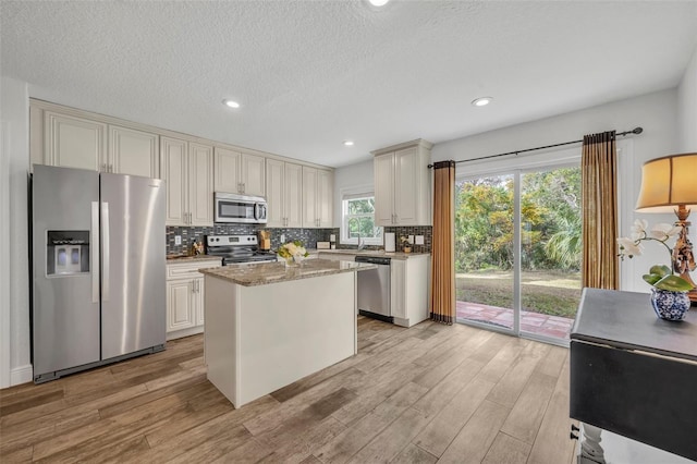 kitchen with sink, light wood-type flooring, a kitchen island, light stone counters, and stainless steel appliances