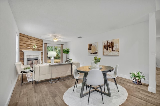 dining space with wooden walls, a fireplace, ceiling fan, and light wood-type flooring