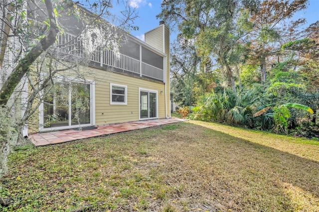 back of property featuring a patio, a lawn, a sunroom, and a chimney