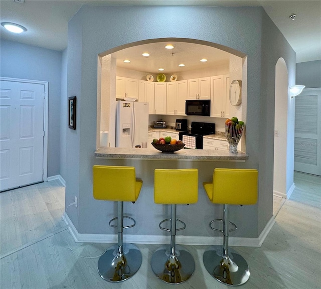 kitchen featuring a kitchen breakfast bar, kitchen peninsula, white cabinets, black appliances, and light wood-type flooring