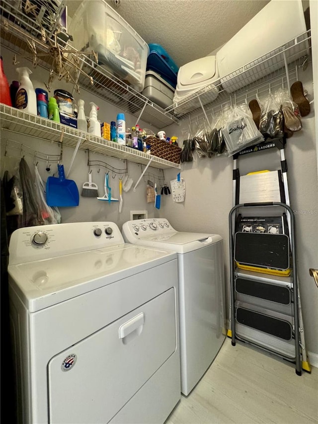 washroom featuring a textured ceiling, light hardwood / wood-style flooring, and washing machine and clothes dryer