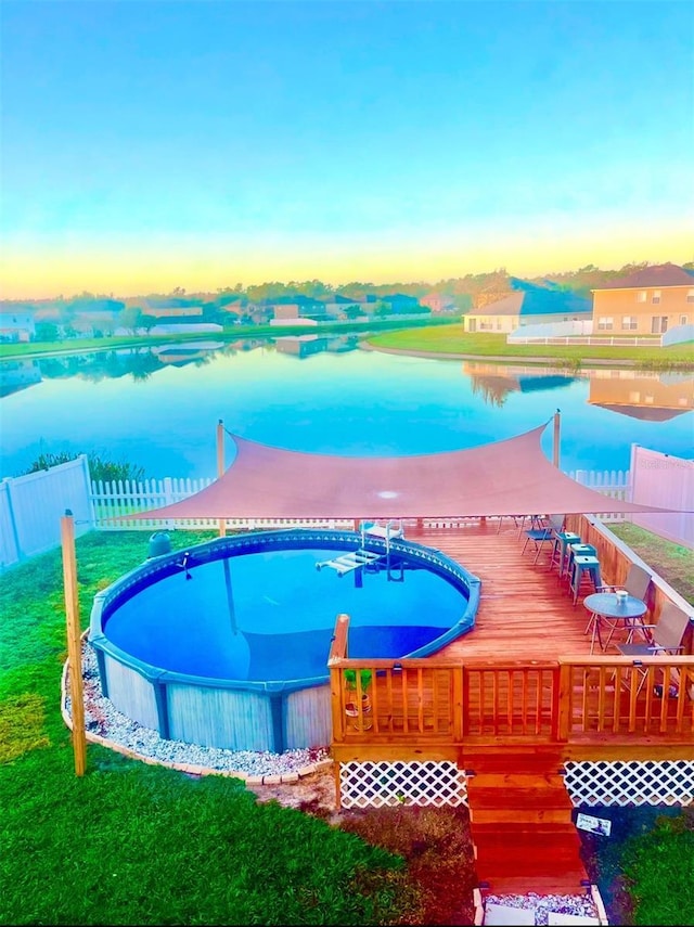 pool at dusk featuring a lawn and a deck with water view