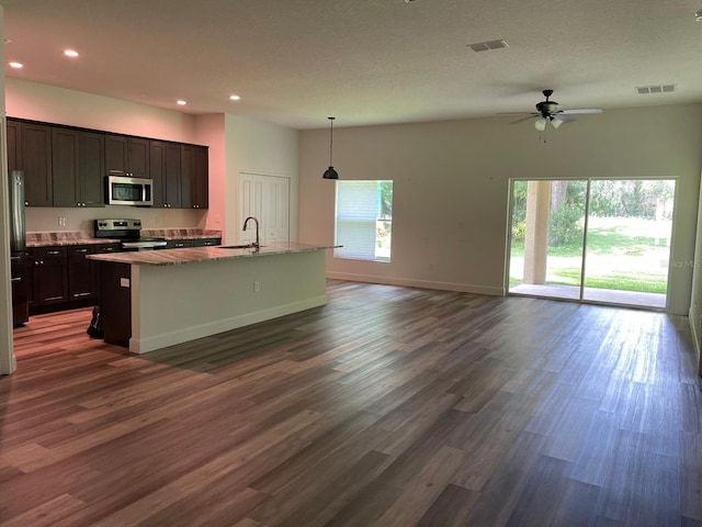 kitchen featuring appliances with stainless steel finishes, ceiling fan, decorative light fixtures, a center island with sink, and dark hardwood / wood-style floors