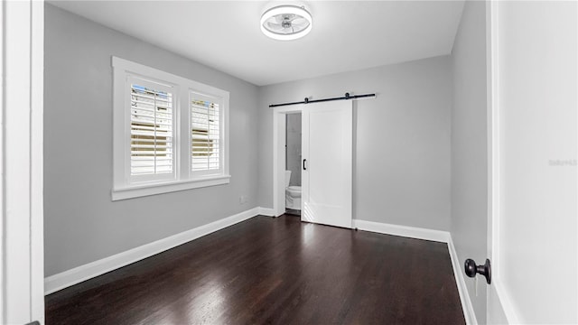 unfurnished bedroom with a barn door, ensuite bath, and dark wood-type flooring