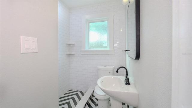 bathroom featuring tiled shower, toilet, tile walls, and sink