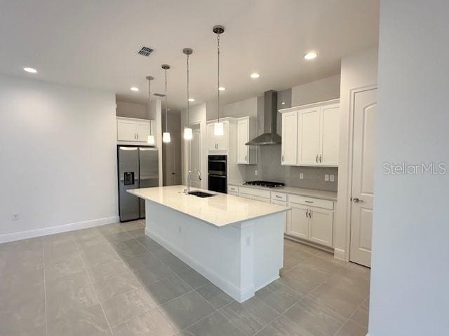 kitchen with pendant lighting, white cabinetry, wall chimney range hood, stainless steel refrigerator with ice dispenser, and a center island with sink