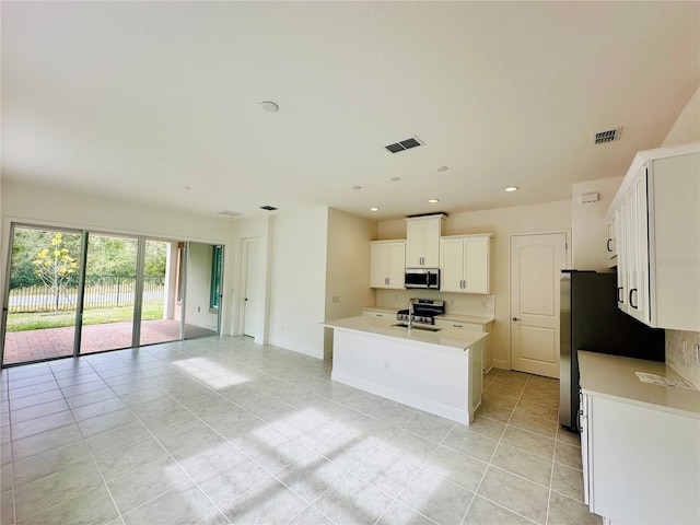 kitchen with appliances with stainless steel finishes, white cabinetry, an island with sink, sink, and light tile patterned floors